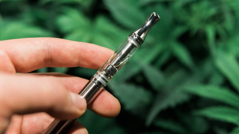 Hand Holding a Vape Pen with THC Oil with Leaves Background