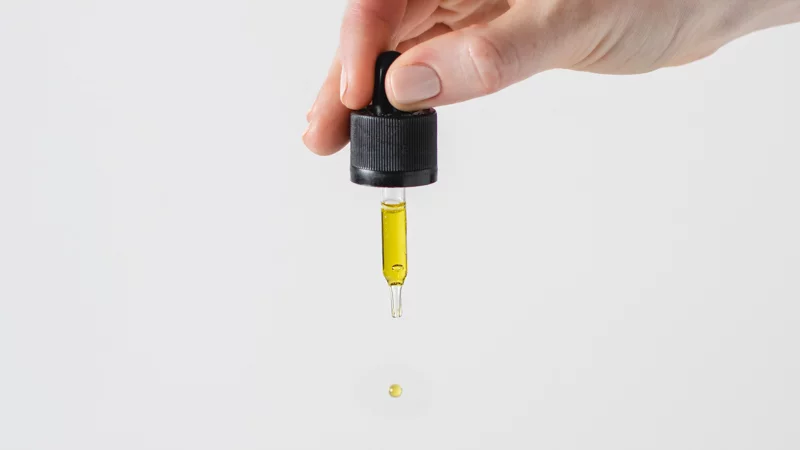 Hand Holding Pipette with THC Oil Dropping on the surface