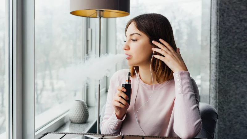 A Lady Vaping With Earphone Sitting Beside the Lampshade