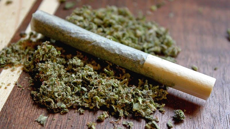 close-up image of hemp cigarette and milled cannabis on a wooden surface