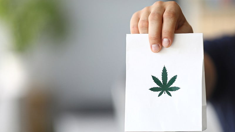 Courier hand holding a paper bag with cannabis logo