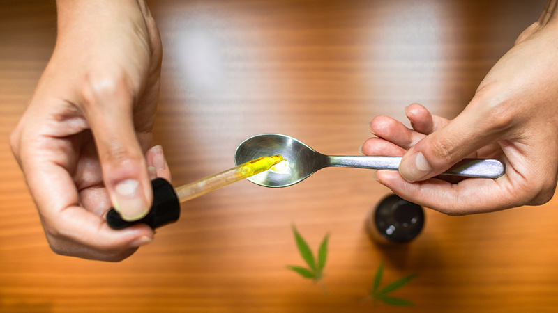 Dosing HHC oil with a dropper with cannabis leaf on the table.