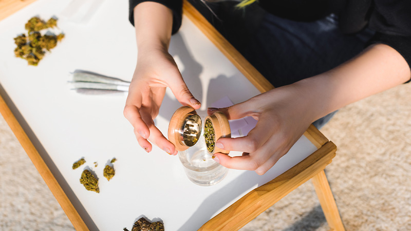 A woman putting ground weed into a glass to for rolling.